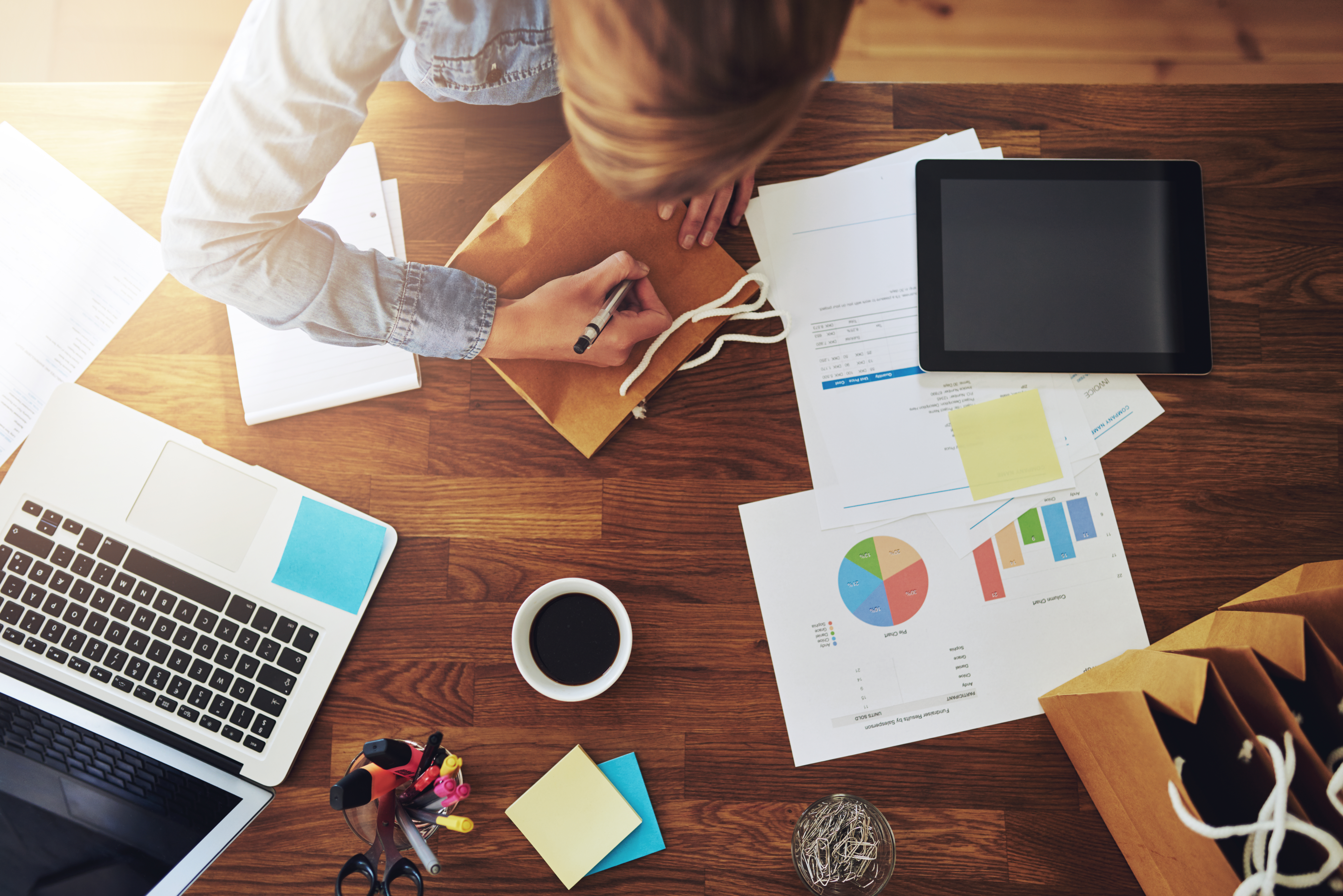 Woman writing surrounded by graphs and a computer.