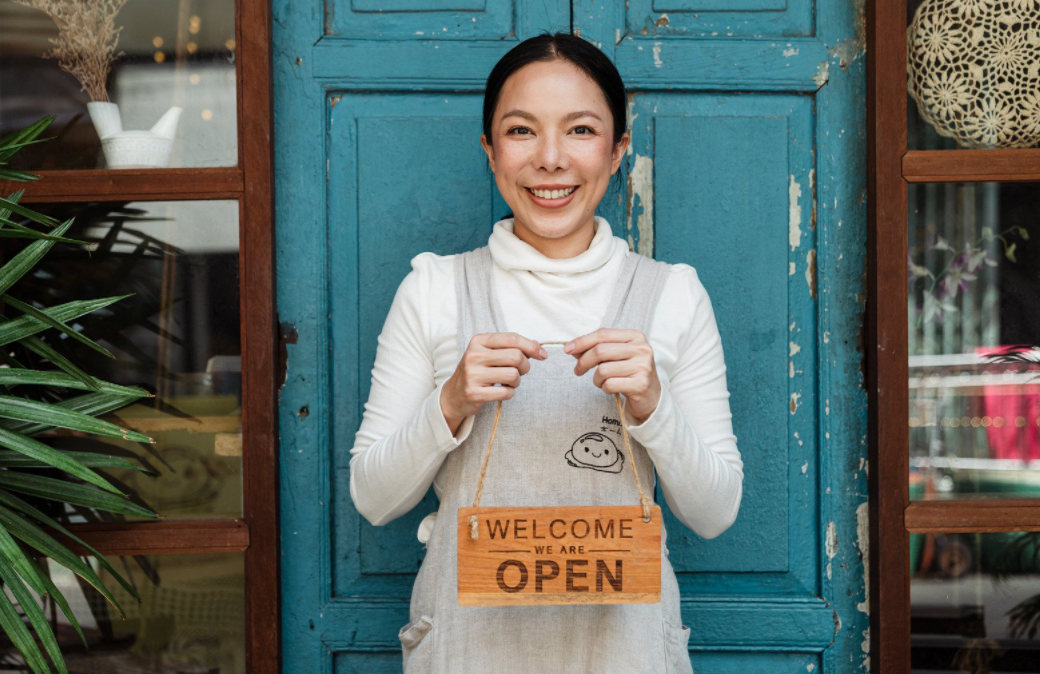 Women standing holding a welcome, we are open sign.