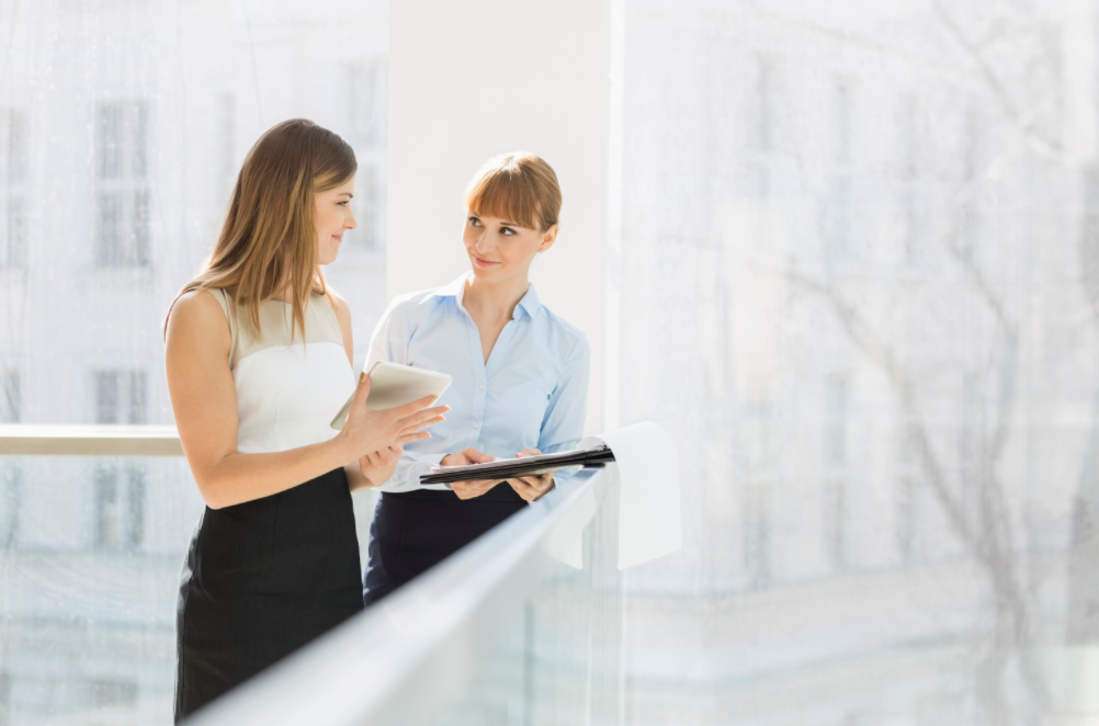 Two women standing and taking notes.