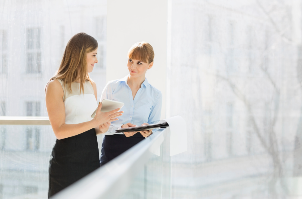 Two women standing and taking notes. 