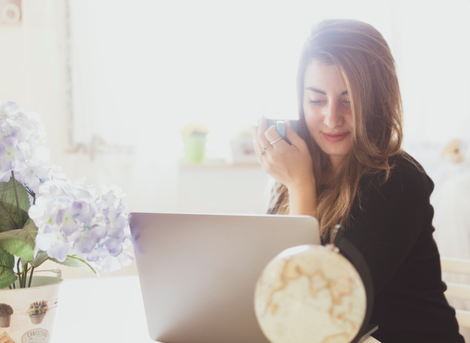 Woman working on laptop holding coffee.