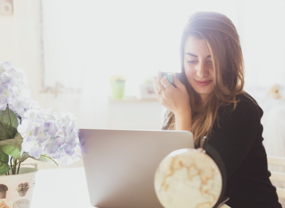 Woman working on laptop holding coffee. 