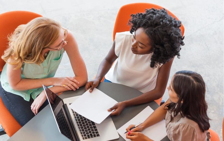 Three women collaborating at a desk | factoring advantages and disadvantages Fundid