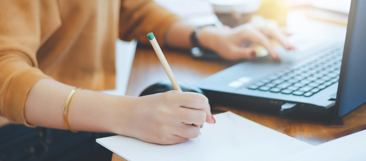 Woman taking notes and using a laptop.